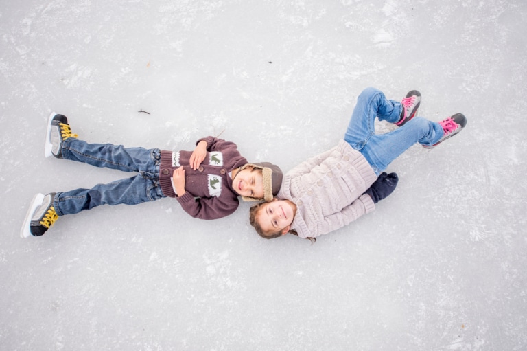 Zwei Kinder mit Schlittschuhen liegen am Eis